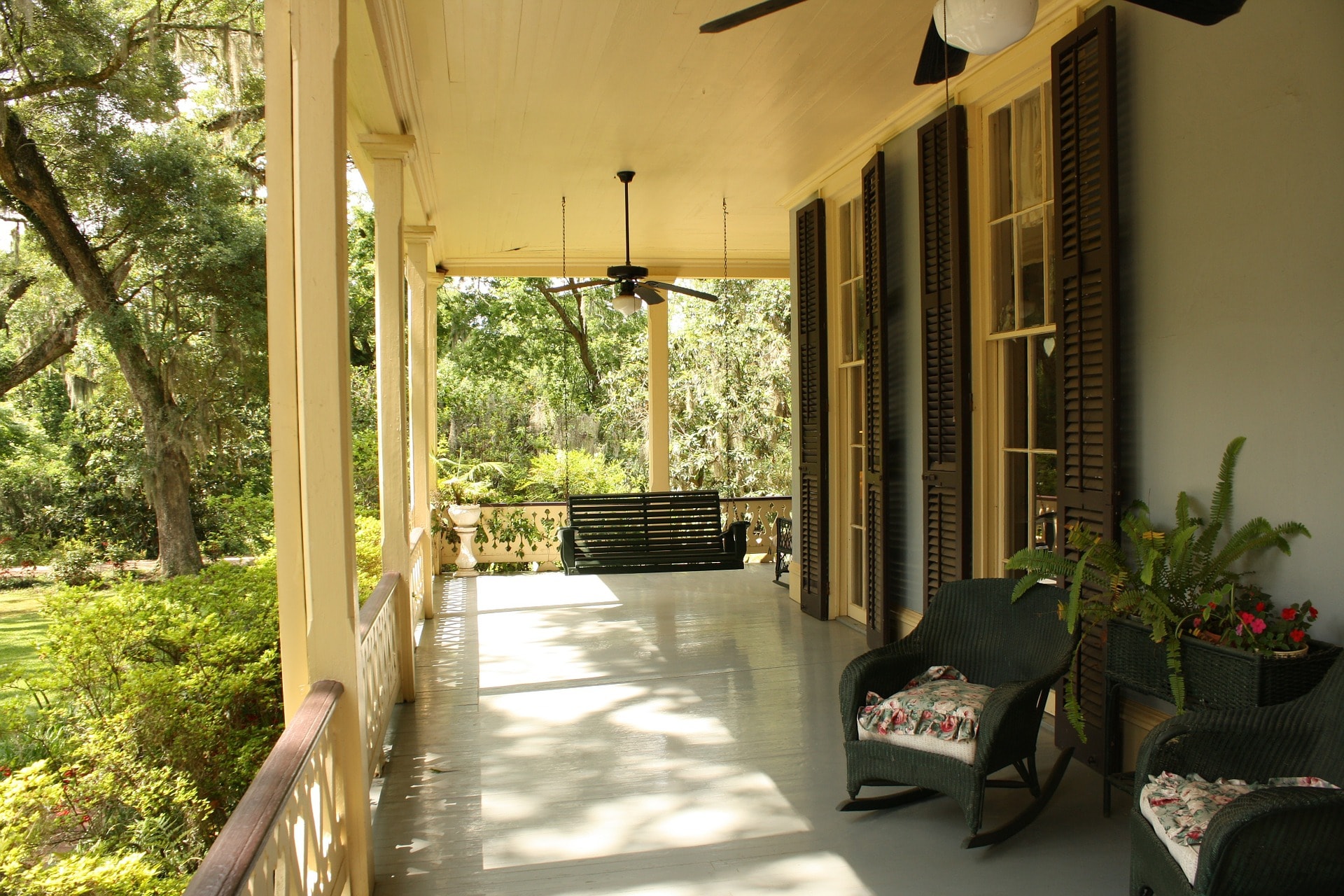 An image of a beautiful porch in a house with chairs,fan and a sceinic view of the greenery around
